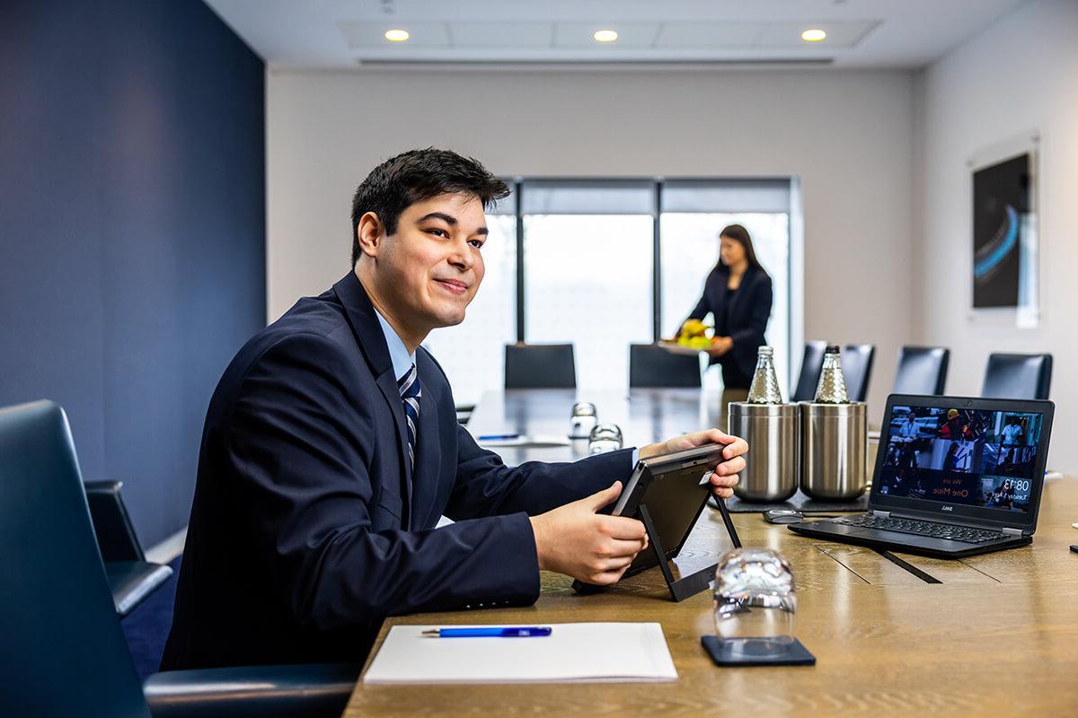 Male front of house employee sitting at a meeting table and helping to set up the technology